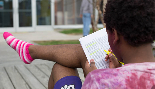 Student in pink socks reads about philosophy on campus.